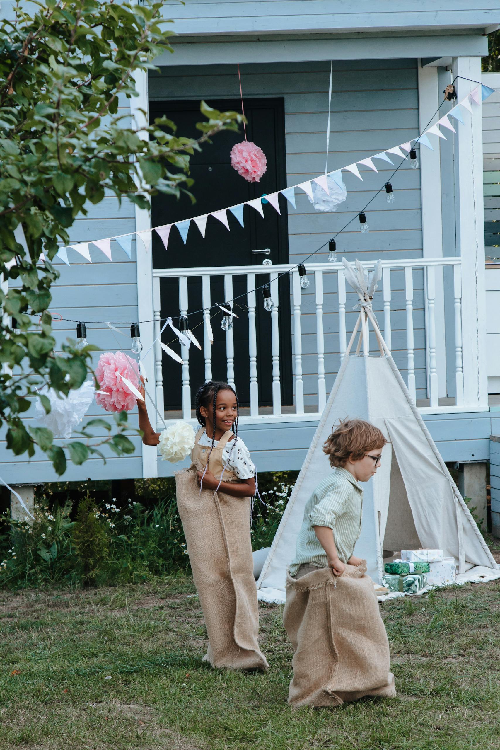 Kids having fun in a sack race at an outdoor party near a cozy house.