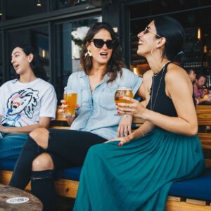 Three friends enjoying drinks and conversation at an outdoor bar.